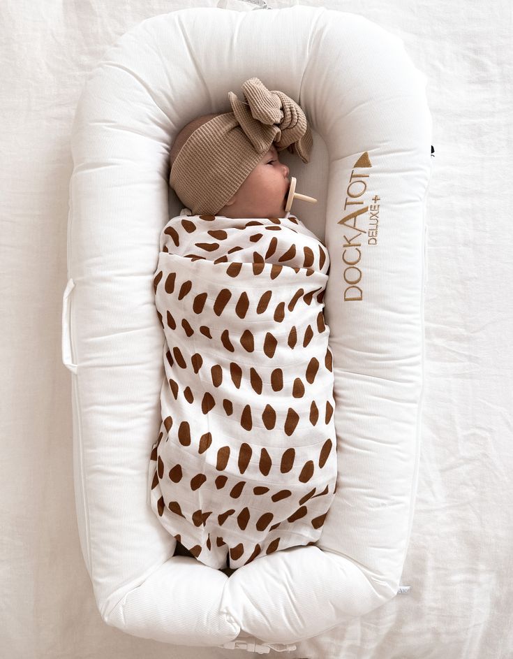 a baby wrapped in a brown and white animal print blanket is sleeping on a pillow