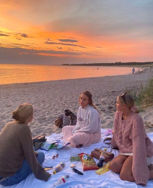 three women are sitting on the beach and having a picnic at sunset or sunrise time