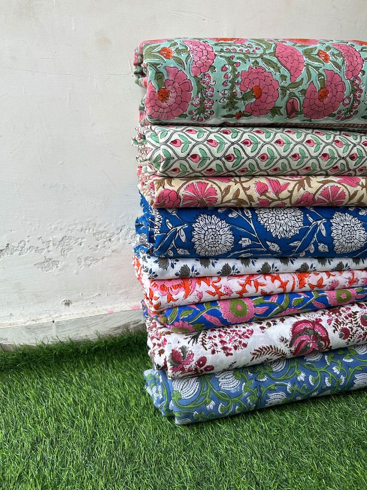 a stack of colorful fabrics sitting on top of green grass next to a white wall