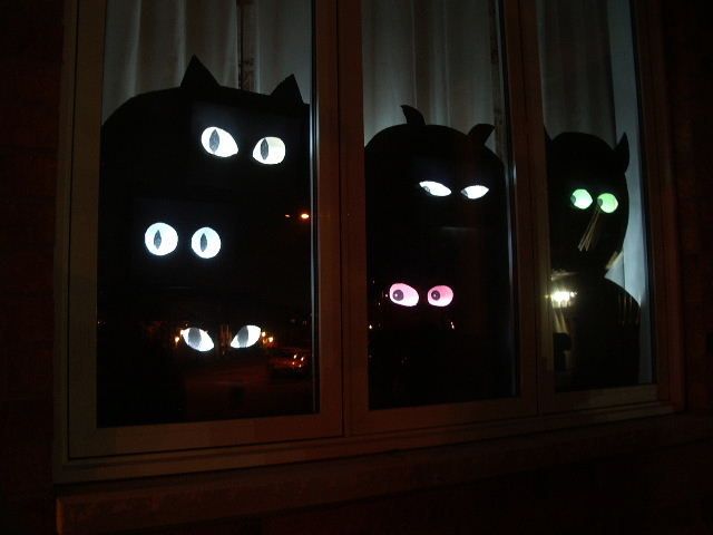 two black cats with glowing eyes are seen through the window