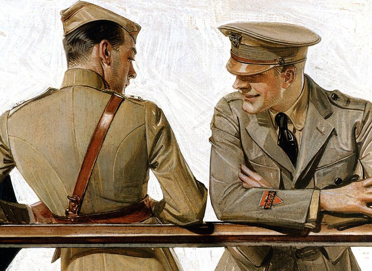 two men in uniforms are sitting at a table and one has his arms crossed as if he is talking to the other man