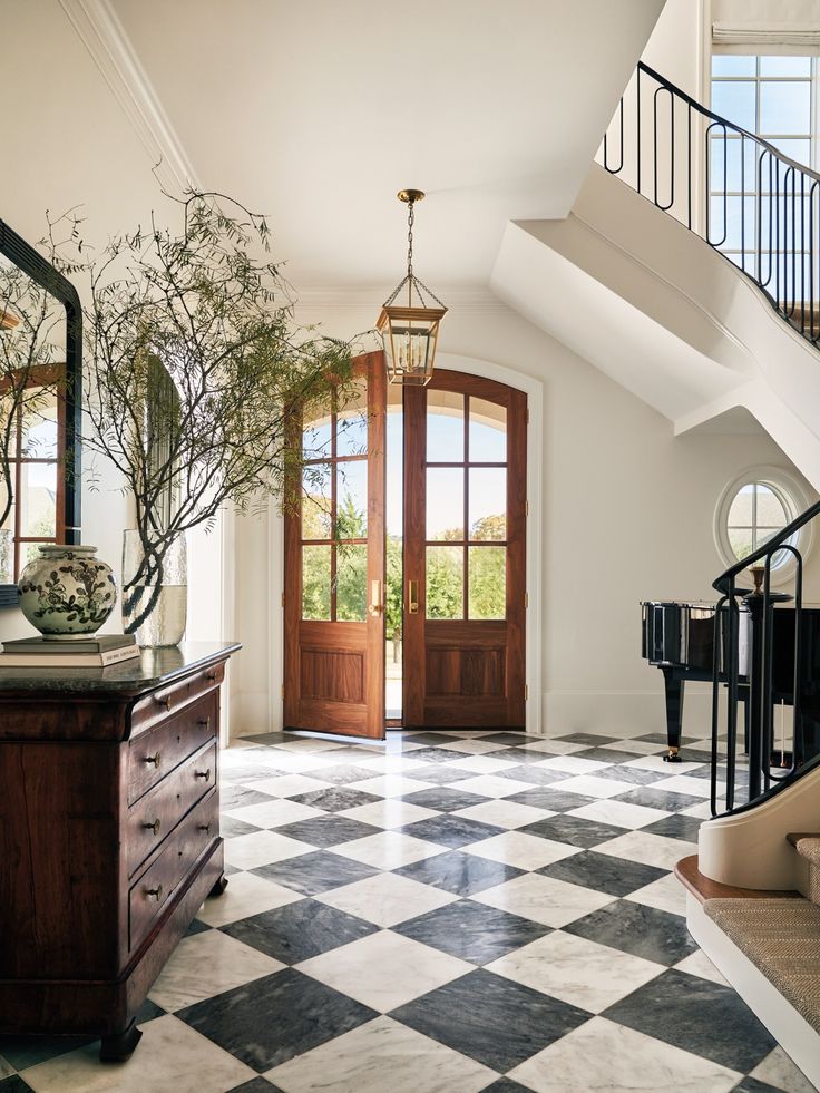 a foyer with black and white checkered flooring, wooden door, and chandelier