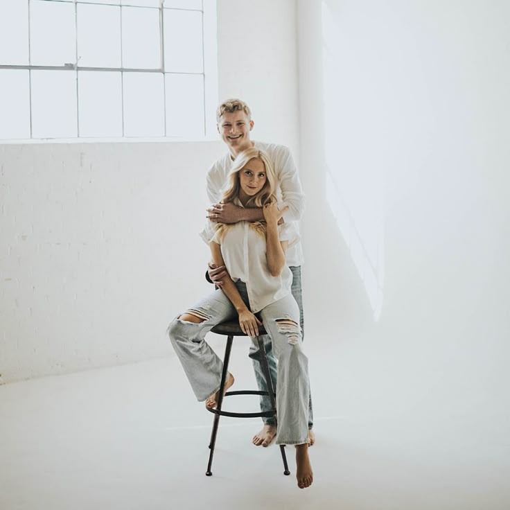 a man and woman sitting on top of a chair in front of a white wall