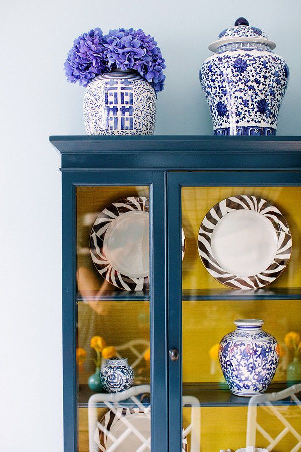 a china cabinet with blue and white dishes on it's glass doors, next to a vase filled with purple flowers