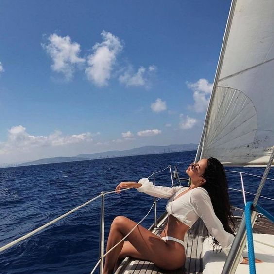 a woman sitting on the deck of a sailboat looking up at the sky and water