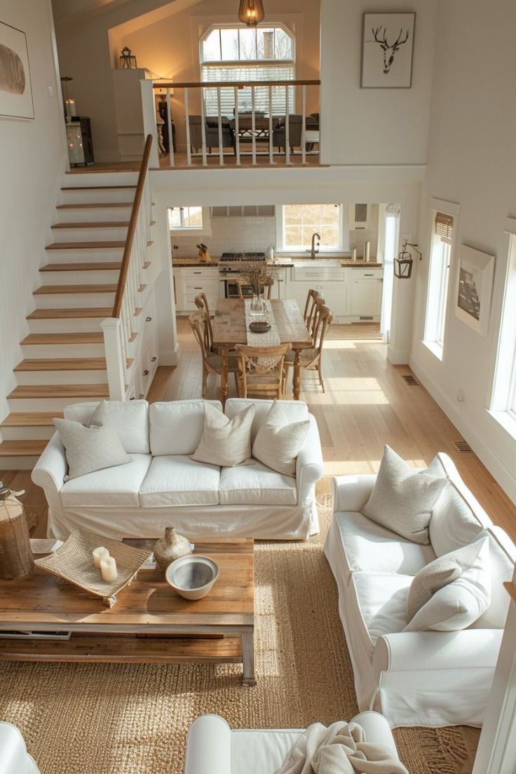 a living room filled with white couches next to a wooden table and staircase leading up to the second floor