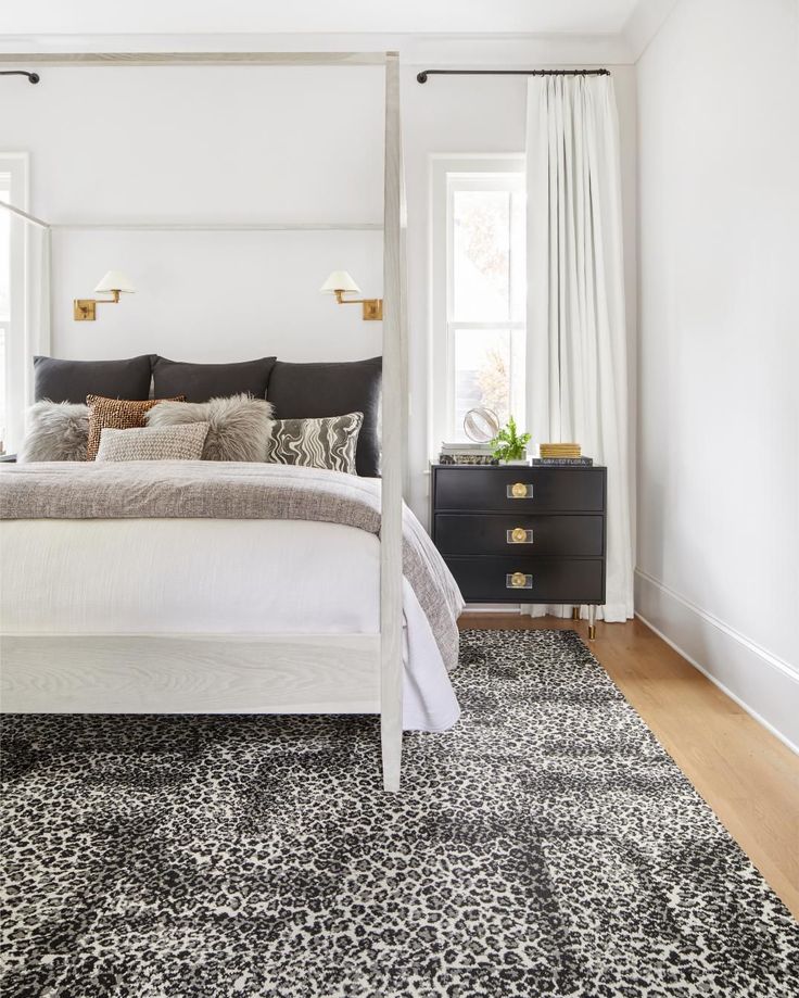 a bedroom with a white bed, black dressers and leopard print rug on the floor