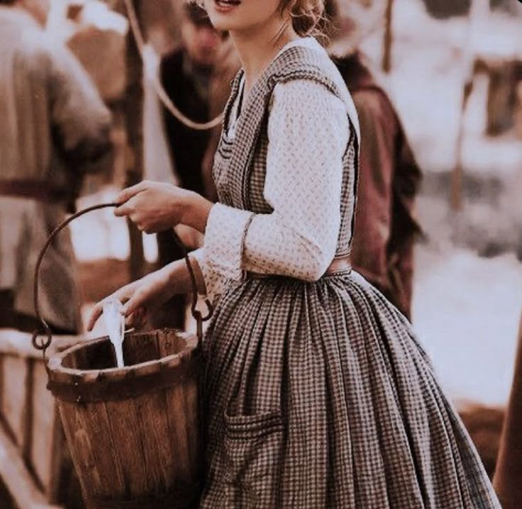 a woman in an old fashioned dress holding a bucket