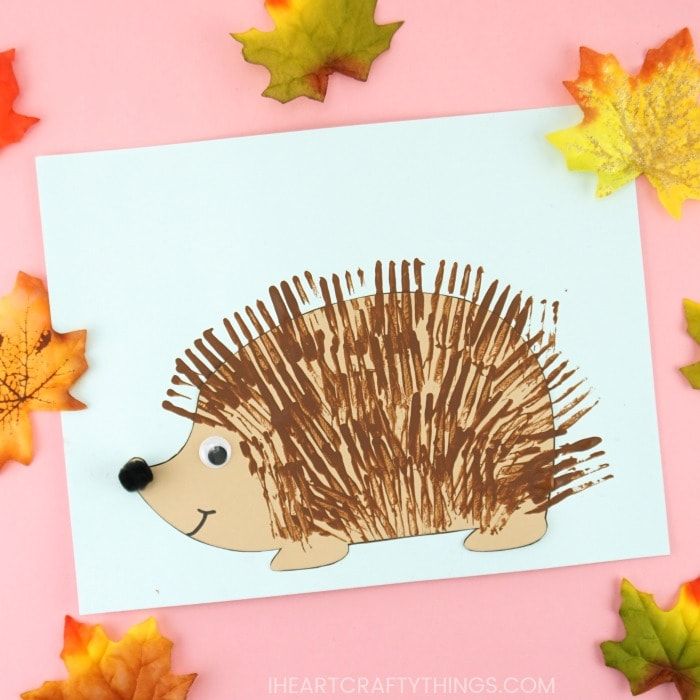 a hedgehog craft with autumn leaves around it on a pink background and a white card