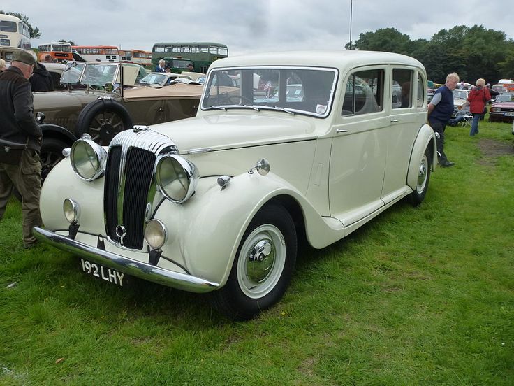 an old white car parked on top of a lush green field next to other cars