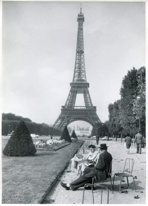 an old photo of a man sitting in front of the eiffel tower, paris