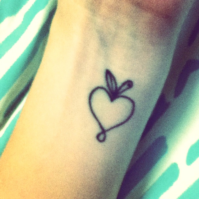 a small heart tattoo on the wrist with an arrow in the shape of a heart