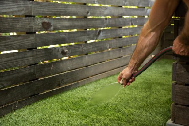 a man is watering the grass with a hose in front of a wooden fence that has been placed on top of it