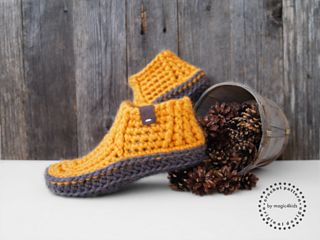 a pair of crocheted slippers sitting next to a pine cone