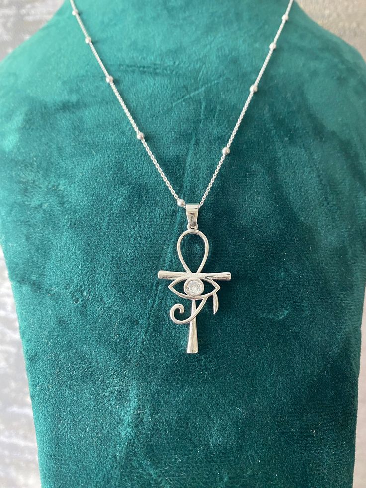 This elegant necklace features a stunning pendant combining two of the most iconic symbols of ancient Egypt: the Ankh and the Eye of Horus. Crafted from high-quality sterling silver, the pendant showcases an intricate design that includes the Eye of Horus set within the loop of the Ankh. The necklace is complemented by a delicate chain adorned with small, evenly spaced beads, adding a touch of sophistication to this unique piece. Perfect for anyone interested in Egyptian mythology or looking for Eye Of Horus Pendant, Eye Of Horus Necklace, The Eye Of Horus, Ankh Necklace, Iconic Symbols, Mystical Jewelry, Real Gold Jewelry, Egyptian Mythology, Jewelry Workshop