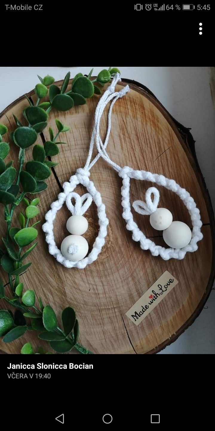 two white beads are hanging from a string on a piece of wood next to some green leaves