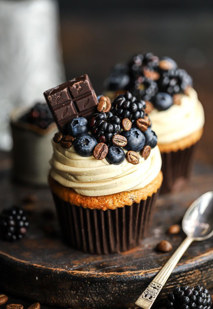 two cupcakes with white frosting and blueberries on top, one topped with chocolate