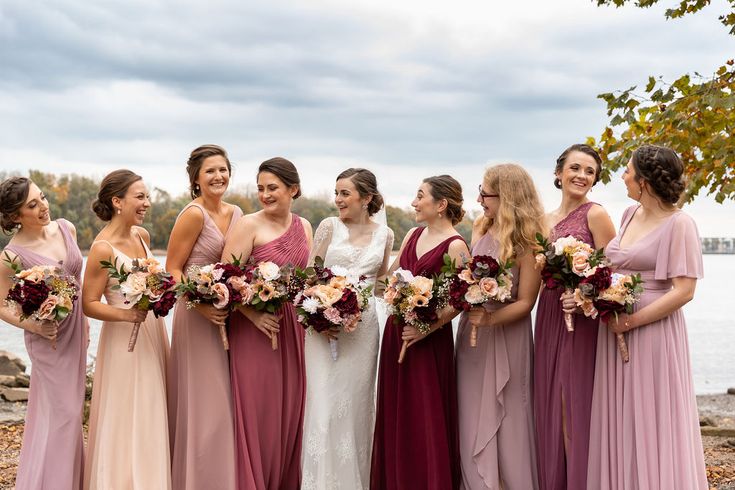 a group of women standing next to each other holding bouquets in their hands and smiling