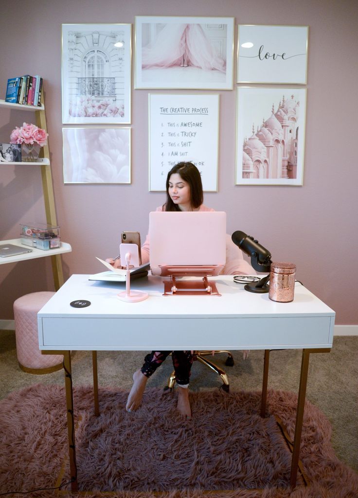 a woman sitting at a desk with a laptop on her lap and pink chair in front of her