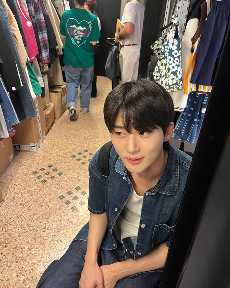 a young man sitting on the ground in front of clothing racks