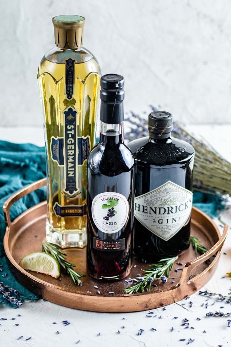 three bottles of liquor sitting on top of a wooden tray next to lavender and rosemary