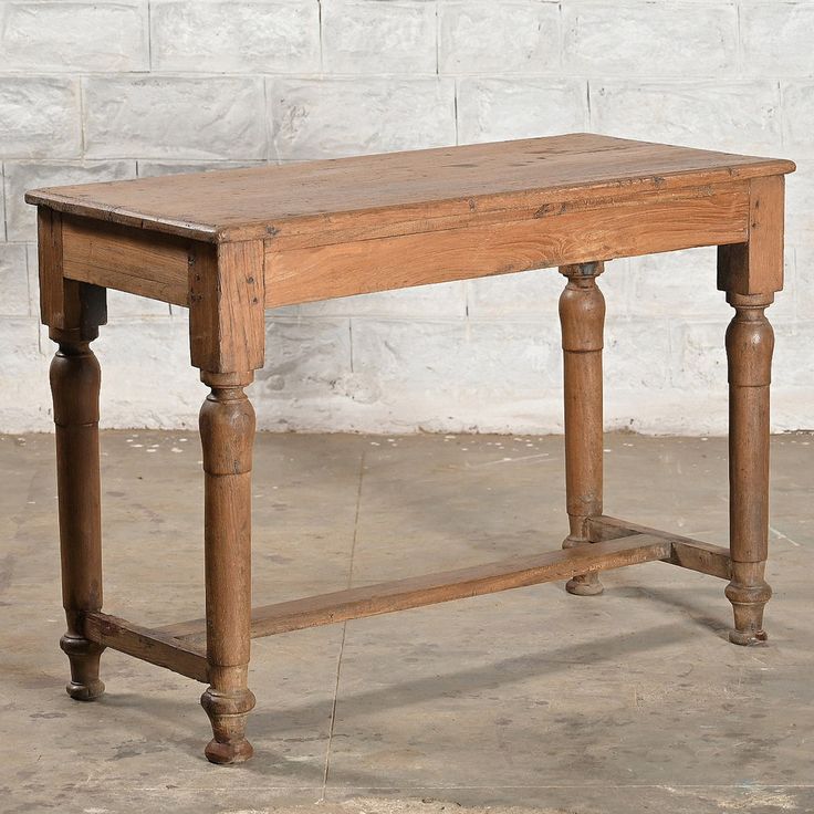 an old wooden table sitting in front of a white brick wall