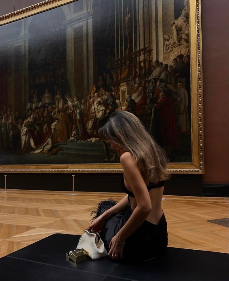 a woman sitting on the floor in front of a painting holding a white purse and looking at it