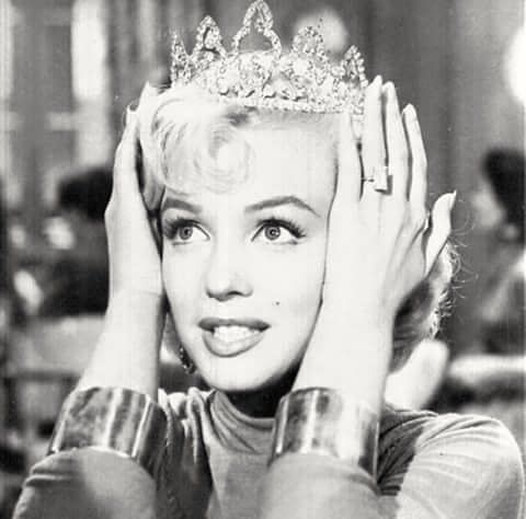 a black and white photo of a woman wearing a tiara with her hands on her head