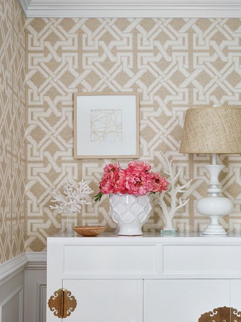 a vase with flowers on top of a white cabinet next to a lamp and wallpaper