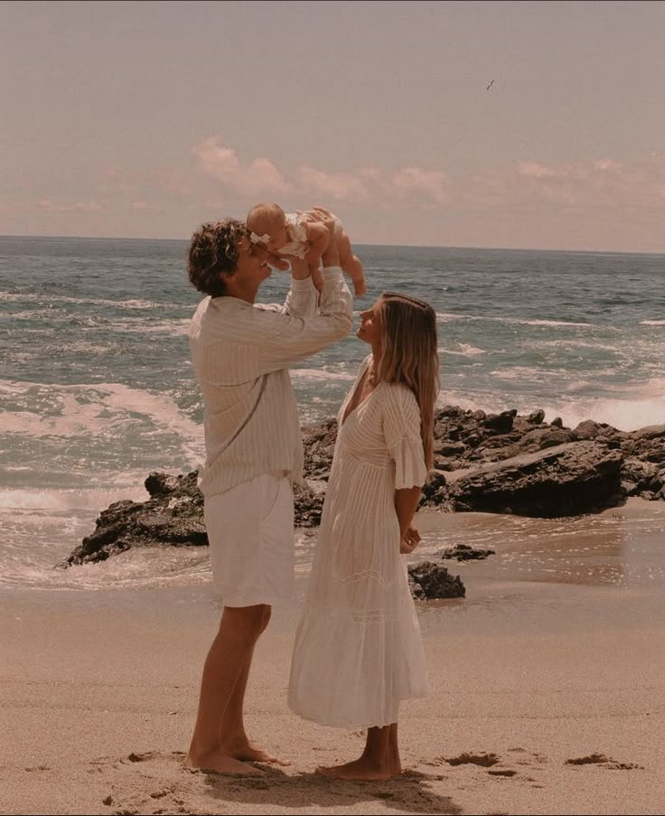 a man holding a baby up to his face while standing next to two women on the beach