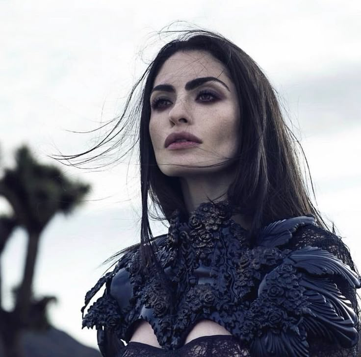 a woman with long dark hair and black gloves on her shoulders is looking off into the distance