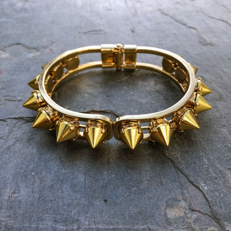 Say hello to your new favorite bracelet. The Helios Cuff is made of gold spikes handset in pronged settings around a hinge closure cuff. The oval shape fits most wrists comfortably and securely, and looks as great solo as it does stacked. DETAILS ✨𝗥𝗘𝗔𝗗𝗬 𝗧𝗢 𝗦𝗛𝗜𝗣✨ Bracelet Diameter: 7” Goth Gold Jewelry, Gold Punk Jewelry, Gold Punk Style Metal Bracelet, Spiked Cuff Bracelet, Edgy Black Metal Cuff Bracelet, Edgy Metal Bracelets With Spikes, Adjustable Punk Cuff Bracelet, Edgy Bracelets, Funky Bracelet