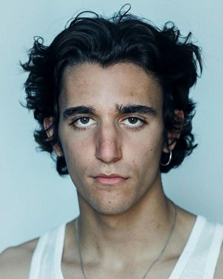 a young man with curly hair wearing a white tank top