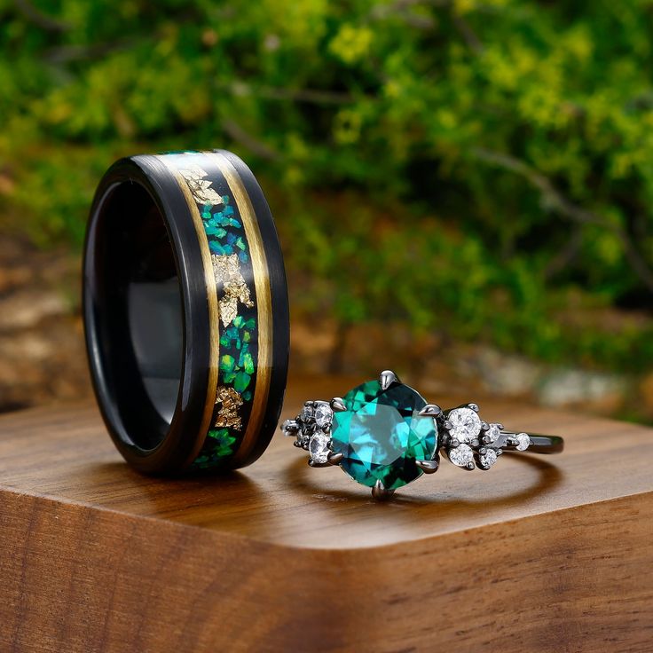 two rings with green and gold in them on top of a wooden table next to some bushes