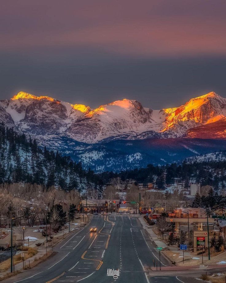 the mountains are covered in snow as the sun is setting on this street and there is no traffic