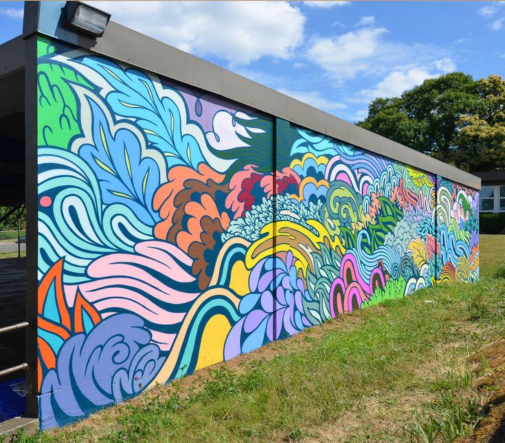 a colorful mural on the side of a building with trees in the back ground and blue sky above