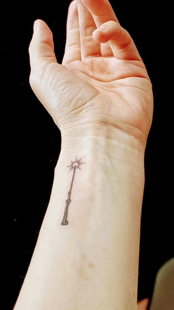 a person's wrist with a small tattoo on the palm tree and an arrow