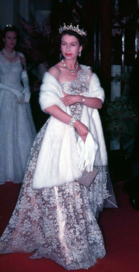 a woman in a white gown and tiara standing on a red carpet with other people