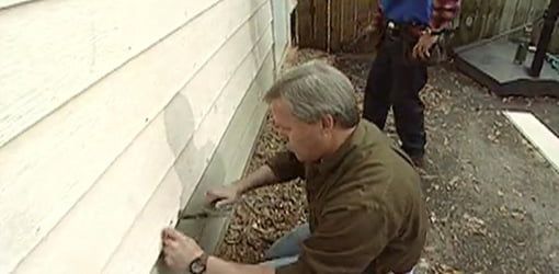 a man is painting the side of a house while another man watches from behind him