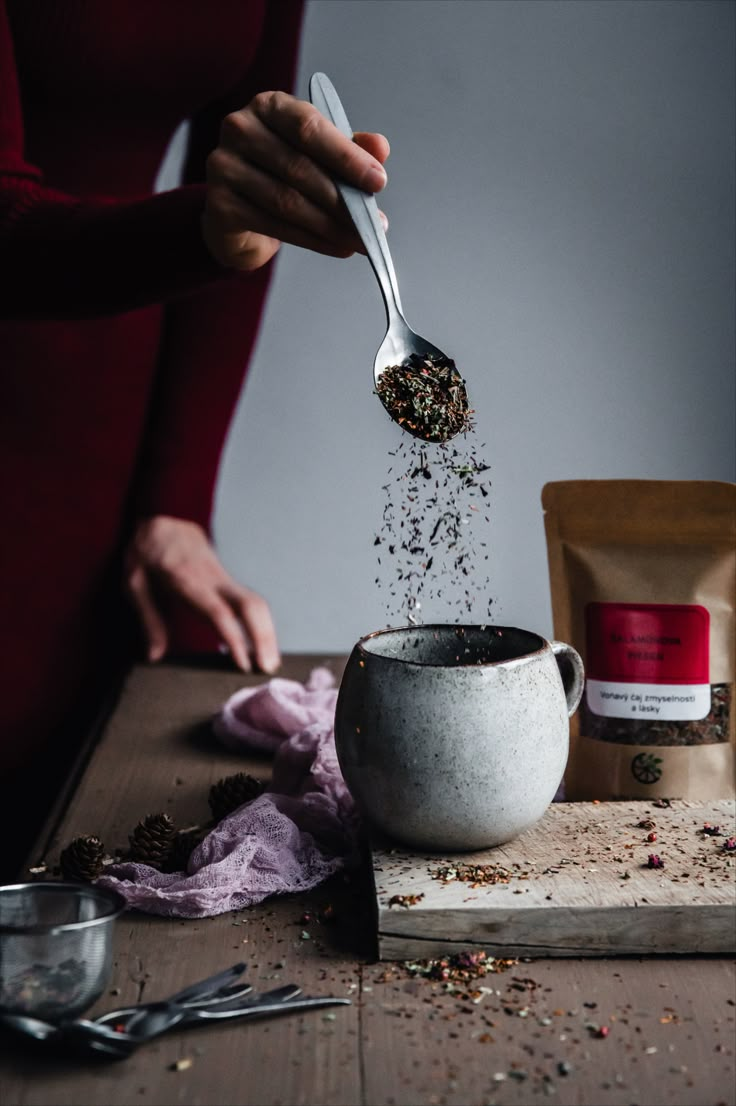 a person pouring tea into a cup on top of a wooden table next to some spoons