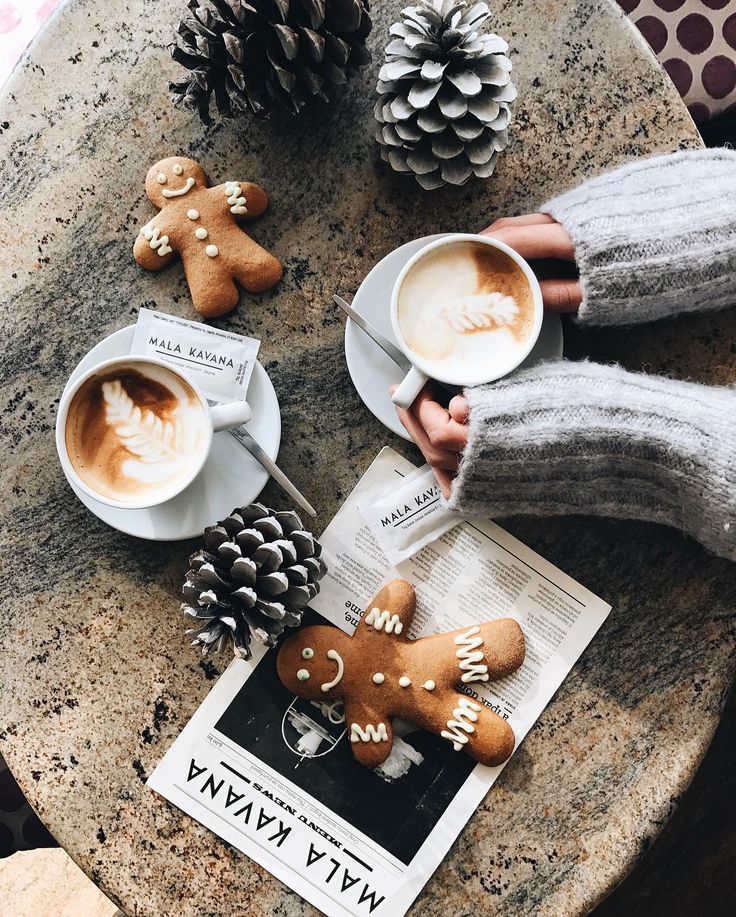 two people holding cups of coffee and ginger cookies on a table with pine cones, fir cones, and other decorations