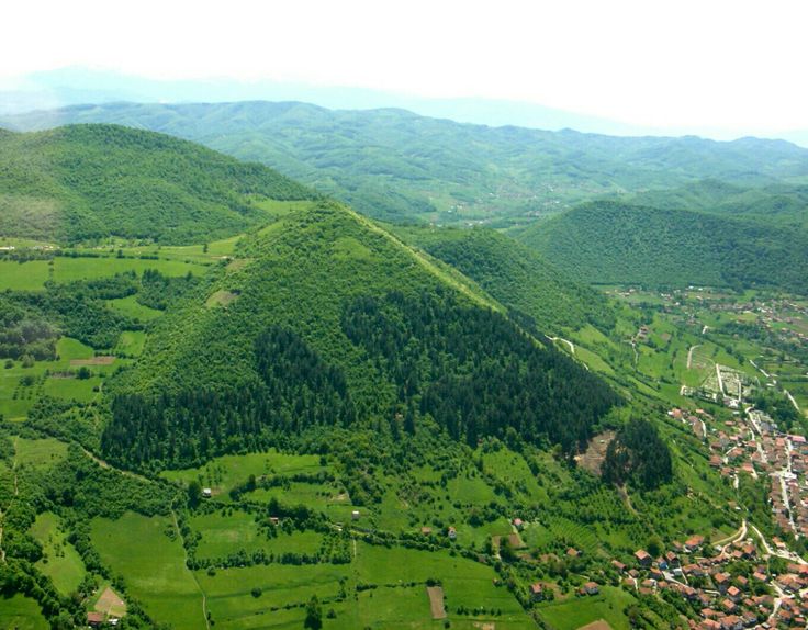 an aerial view of a green valley with mountains in the background