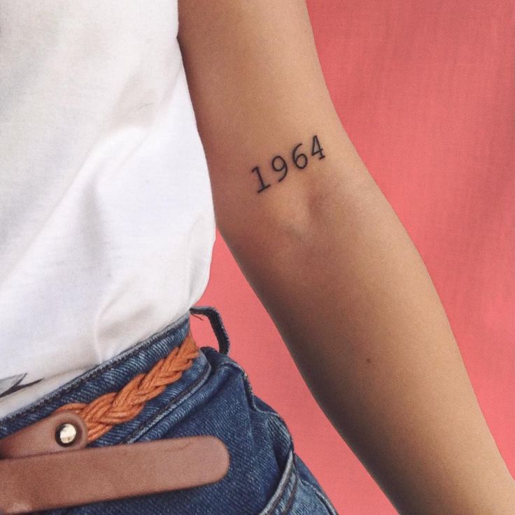 a woman's arm with a tattoo on it that reads, 1994 and has an orange braid