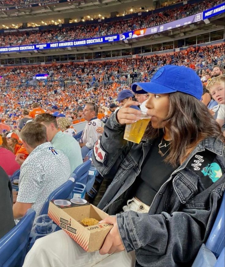 a woman sitting in the bleachers with a box of popcorn and a drink