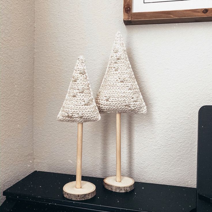 two knitted christmas trees sitting on top of a black shelf