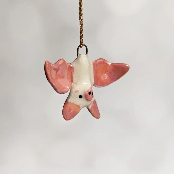 a pink and white ceramic bird ornament hanging from a gold chain