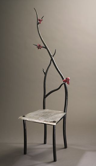 a chair made out of branches with flowers on the back and seat, sitting in front of a gray background