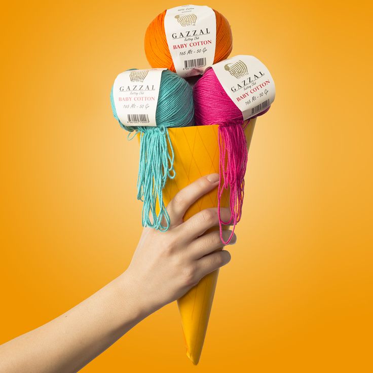 a hand holding a cone filled with yarn and crochet hooks on an orange background