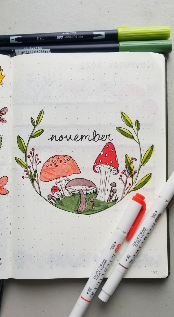 an open notebook with mushrooms and leaves on the cover, next to two marker pens