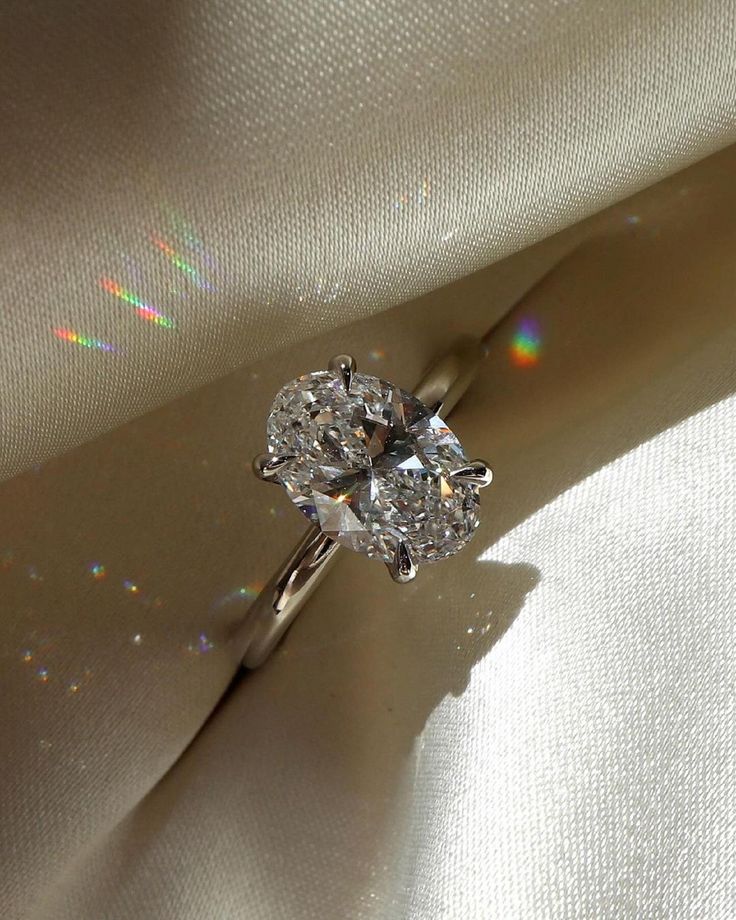 a diamond ring sitting on top of a white satin material covered in light shining from the sun